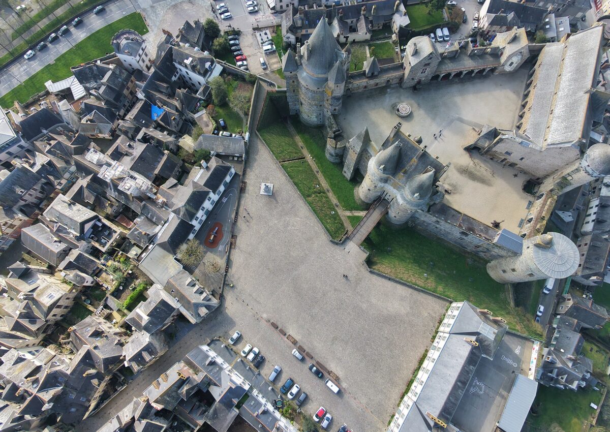 Le château de Vitré photographié par drone en 2026, sous le même angle, devant une esplanade sablée entièrement dégagée